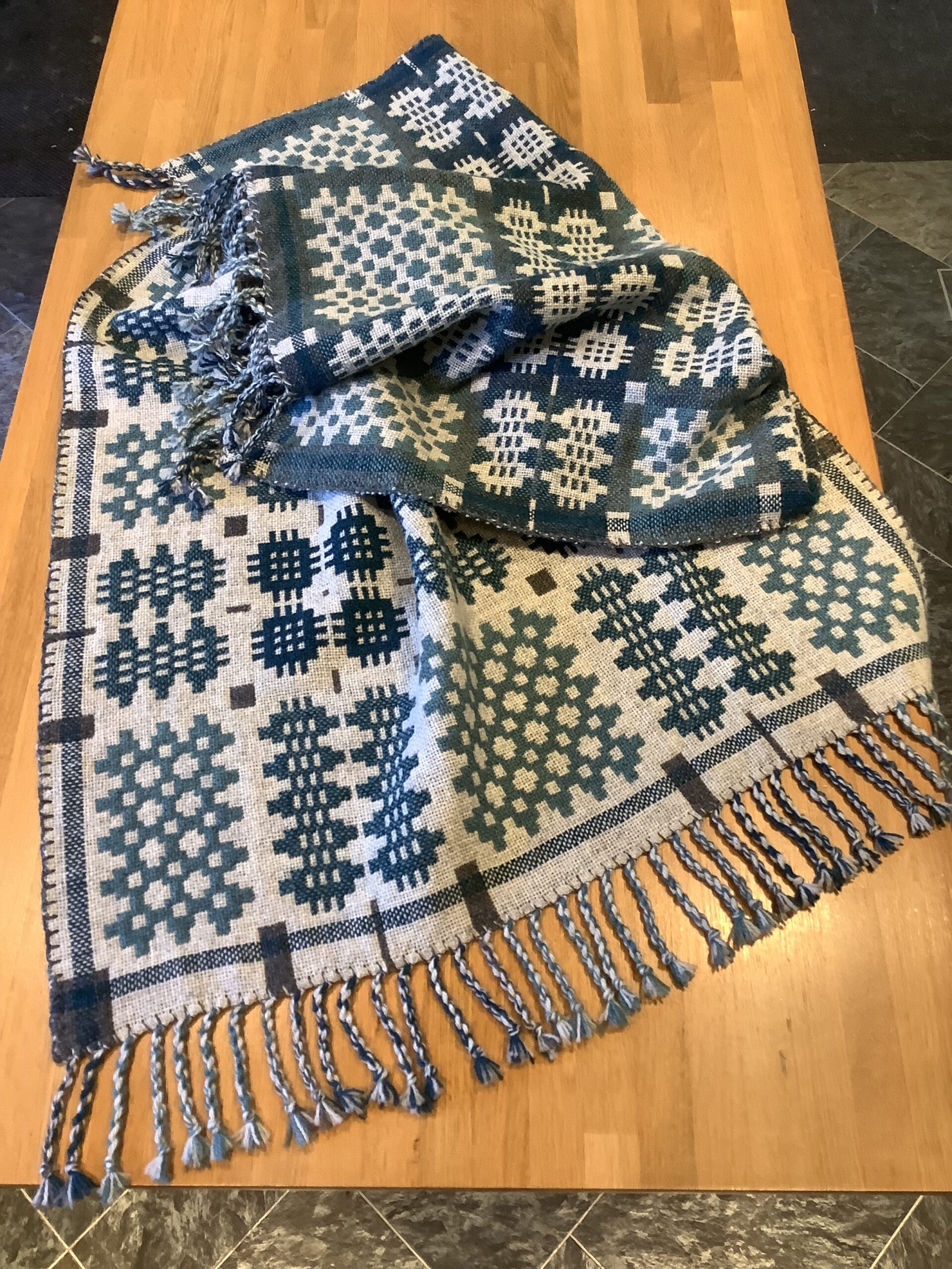The finished blanket laid on a table. The warp ends have been tied into tassels. The finished blanket laid on a table. The warp ends have been tied into tassels.